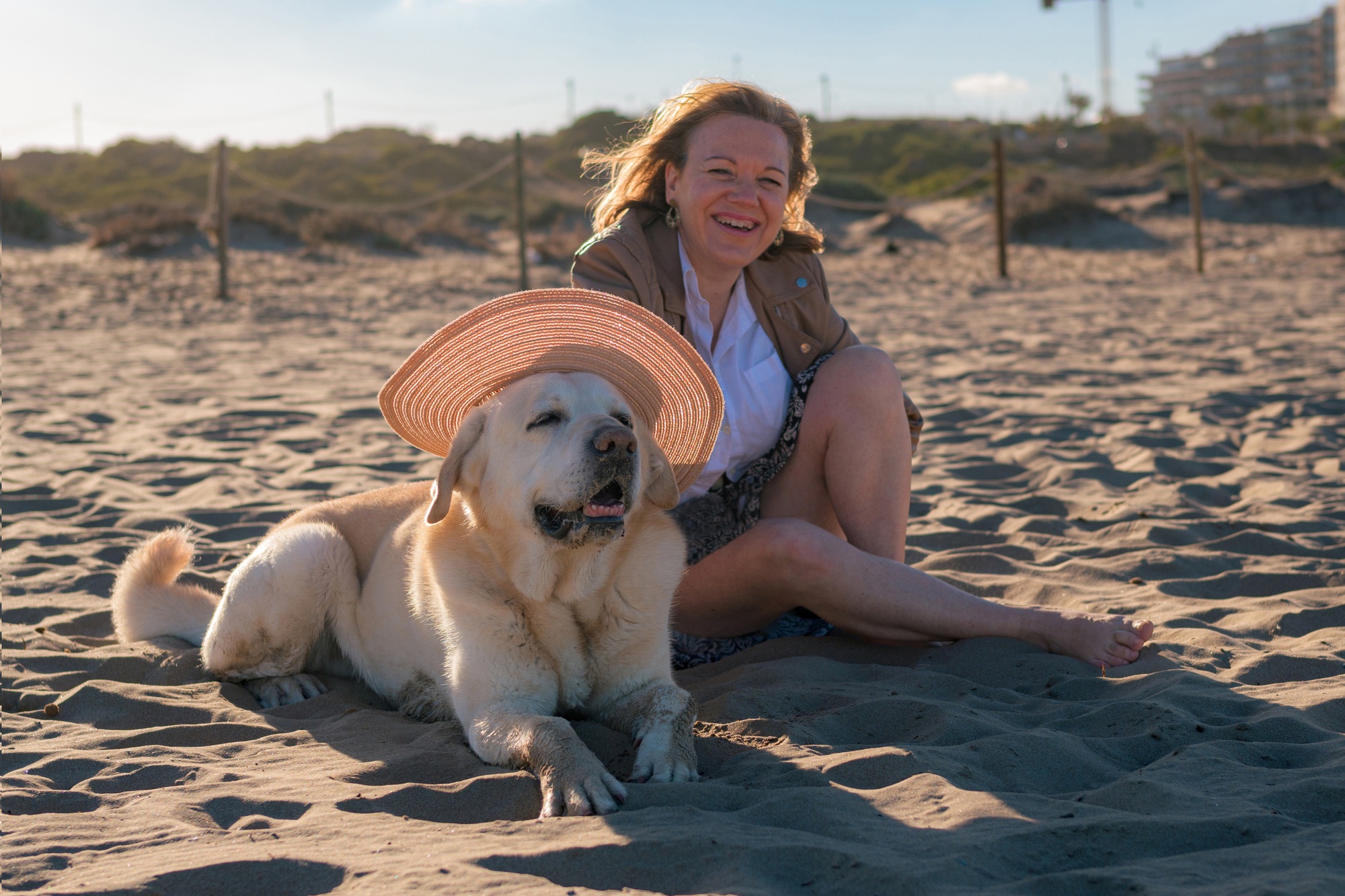 Woman enjoys putting a hat on her dog at the beach